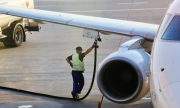 Airport worker in safety vest refueling a plane wing from a fuel truck, highlighting aviation maintenance.