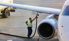 Airport worker in safety vest refueling a plane wing from a fuel truck, highlighting aviation maintenance.