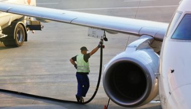 Airport worker in safety vest refueling a plane wing from a fuel truck, highlighting aviation maintenance.