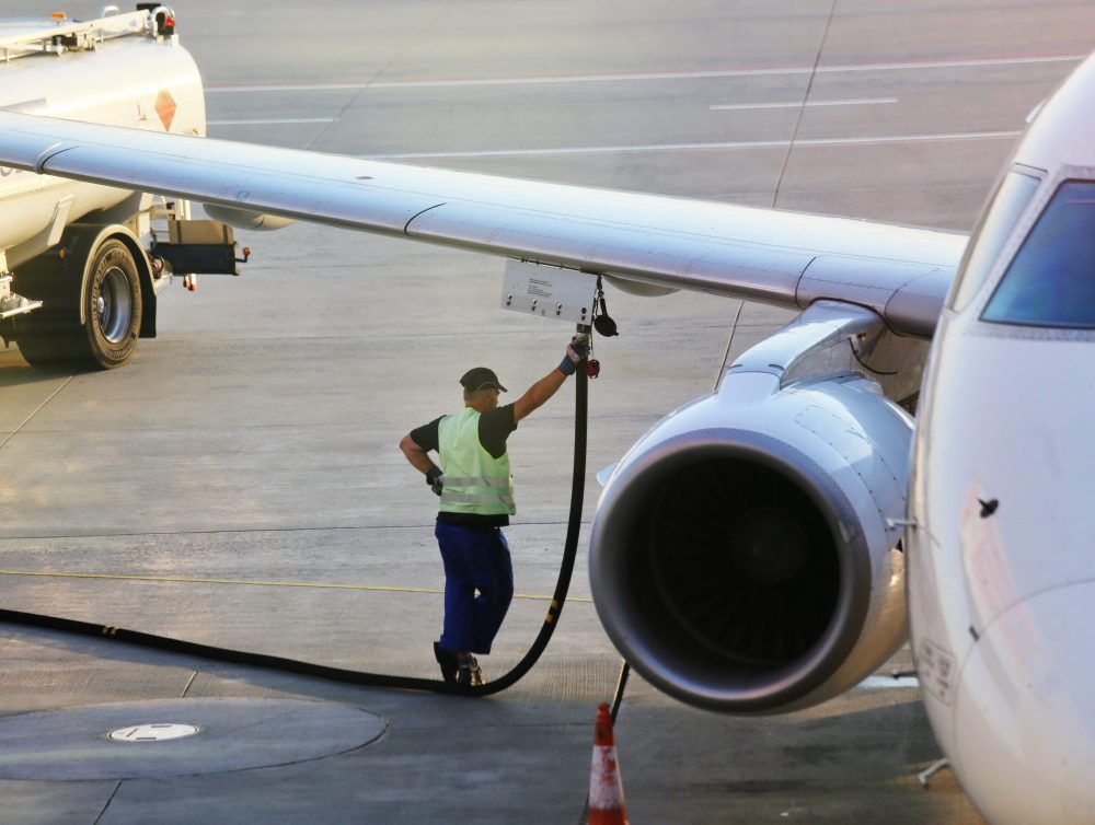 Airport worker in safety vest refueling a plane wing from a fuel truck, highlighting aviation maintenance.